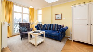 A living room with a sofa, armchair, and coffee table, a window with curtains, a framed picture on the wall, and a wardrobe. - The Villa, App. 8, Germany (Heringsdorf)