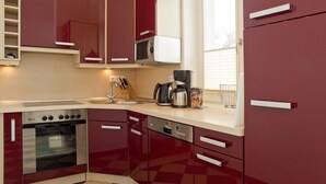 A kitchen with red cabinets, a stove, a microwave, and a coffee maker.