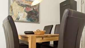 A dining area with a wooden table, black leather chairs, a woven basket, and a painting on the wall.