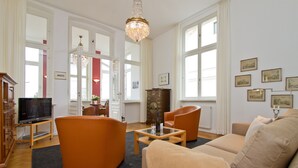 A spacious living room with a large window, a chandelier, and a television.