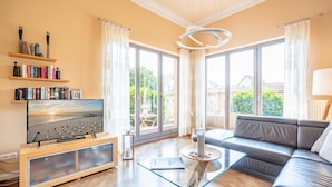 Uma sala de estar moderna com um sofá de couro, uma mesa de centro de vidro e uma televisão de tela plana em um suporte de madeira.