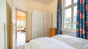 Quarto com cama, guarda-roupa, penteadeira e janela com cortinas.