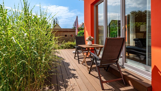 Um deck de madeira com móveis de exterior, um vaso de planta e uma porta de correr de vidro que dá para um quarto.