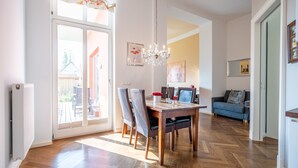Uma sala de jantar com uma mesa e cadeiras de madeira, um candelabro e vista para o exterior através de uma porta de vidro.