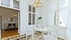 Ein Essbereich mit einem weißen Tisch, vier gestreiften Stühlen, einer Chandelierleuchtreiter und Blick auf ein Wohnzimmer mit einer Couch und einem Schrank.