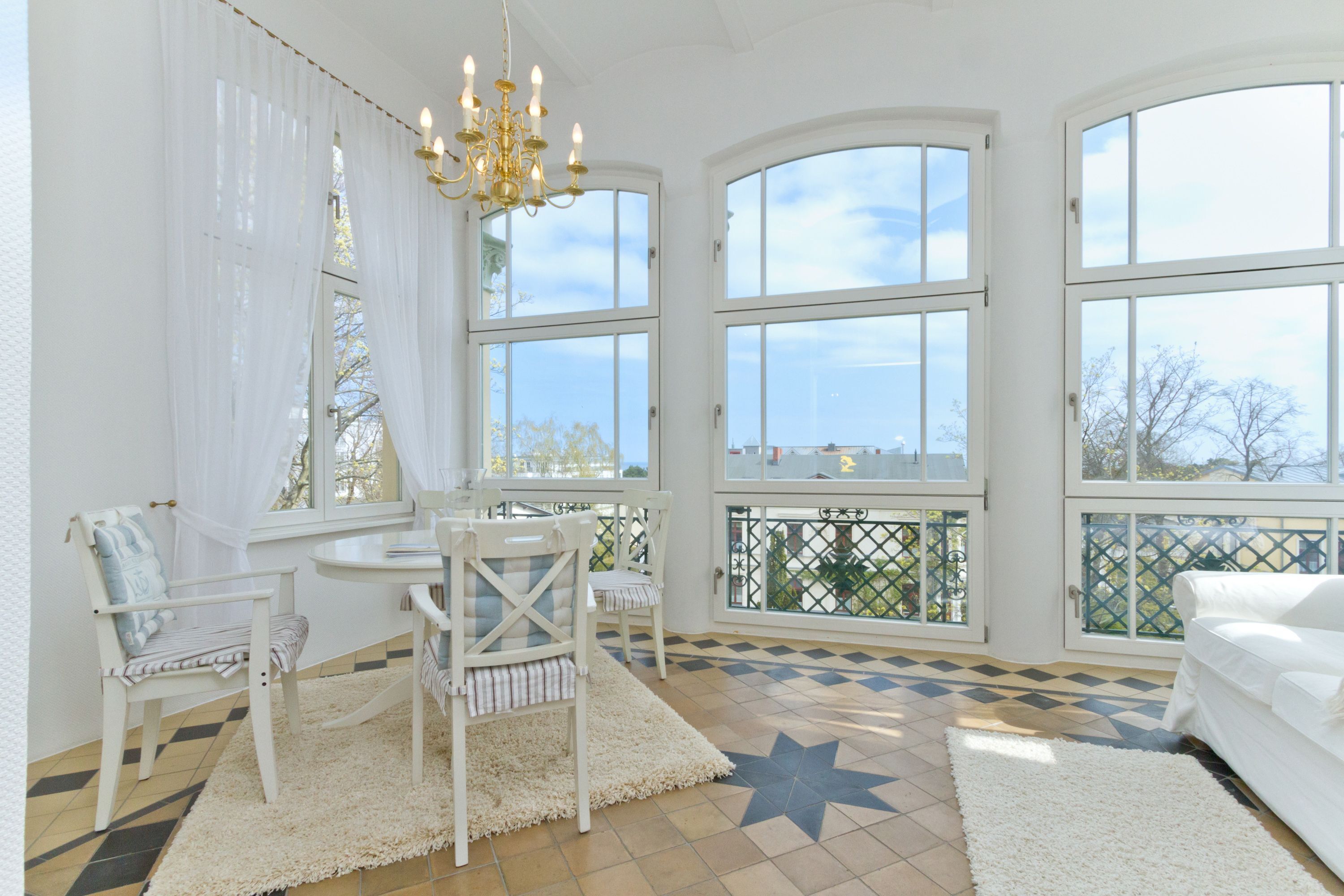 A bright room with large windows, a chandelier, and a white sofa.