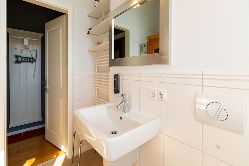 Une salle de bain avec un lavabo blanc, un miroir au-dessus et une porte sur laquelle est inscrit le mot « PLAGE ».