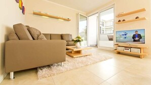 A modern living room with a sofa, a coffee table, a TV, and a large window. - Stadtvilla Blumenhof, App. 6 (Heringsdorf)
