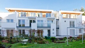 A modern multi-story residential building with balconies, a small garden area, and a clear sky. - Stadtvilla Blumenhof, App. 6 (Heringsdorf)