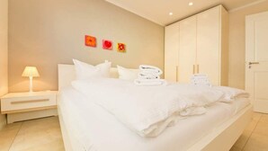 A hotel room with a large bed, white linens, a nightstand with a lamp, and a wardrobe. - Stadtvilla Blumenhof, App. 6 (Heringsdorf)