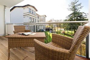 Ein Balkon mit Korbmöbeln, Blick auf ein Haus und einen Baum.