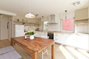 Una cocina moderna con armarios blancos, una mesa de comedor de madera e iluminación colgante.