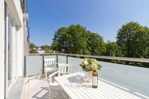 Ein Balkon mit einem weißen Tisch, zwei Stühlen, einer Weinflasche und einem Blumenstrauß.