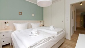 A hotel room with two beds, a white nightstand, a wall-mounted lamp, and a door leading to another room.
