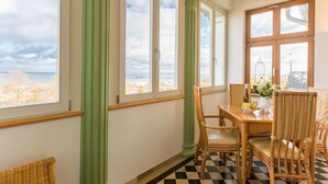 Uma área de refeições com mesa e cadeiras, janelas amplas com cortinas e vista para o exterior.