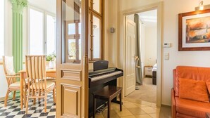 Uma sala de estar com um piano, um espaço de jantar com cadeiras, um sofá e um quadro na parede.