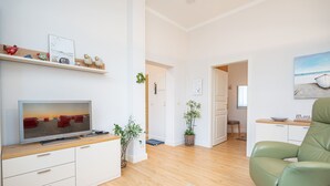 A modern living room with a flat-screen TV, a green sofa, and a wooden floor. - Villa Belvedere, App. 03 (Heringsdorf)