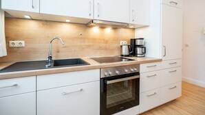 A modern kitchen with white cabinets, a stainless steel sink, a built-in oven, and a coffee maker. - Villa Belvedere, App. 03 (Heringsdorf)