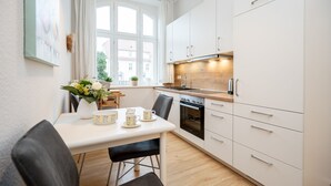 A modern kitchen with white cabinets, a wooden countertop, and a dining area with a table set for two. - Villa Belvedere, App. 03 (Heringsdorf)