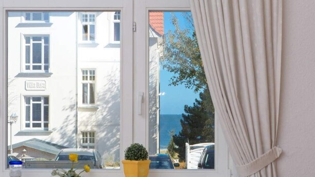 A window with a view of a building labeled "Villa Deza" and a small potted plant on the windowsill. - Villa Belvedere, App. 03 (Heringsdorf)