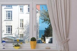 Una finestra amb vista a un edifici anomenat "Villa Deza" i una petita planta en test amb flor a la finestra.