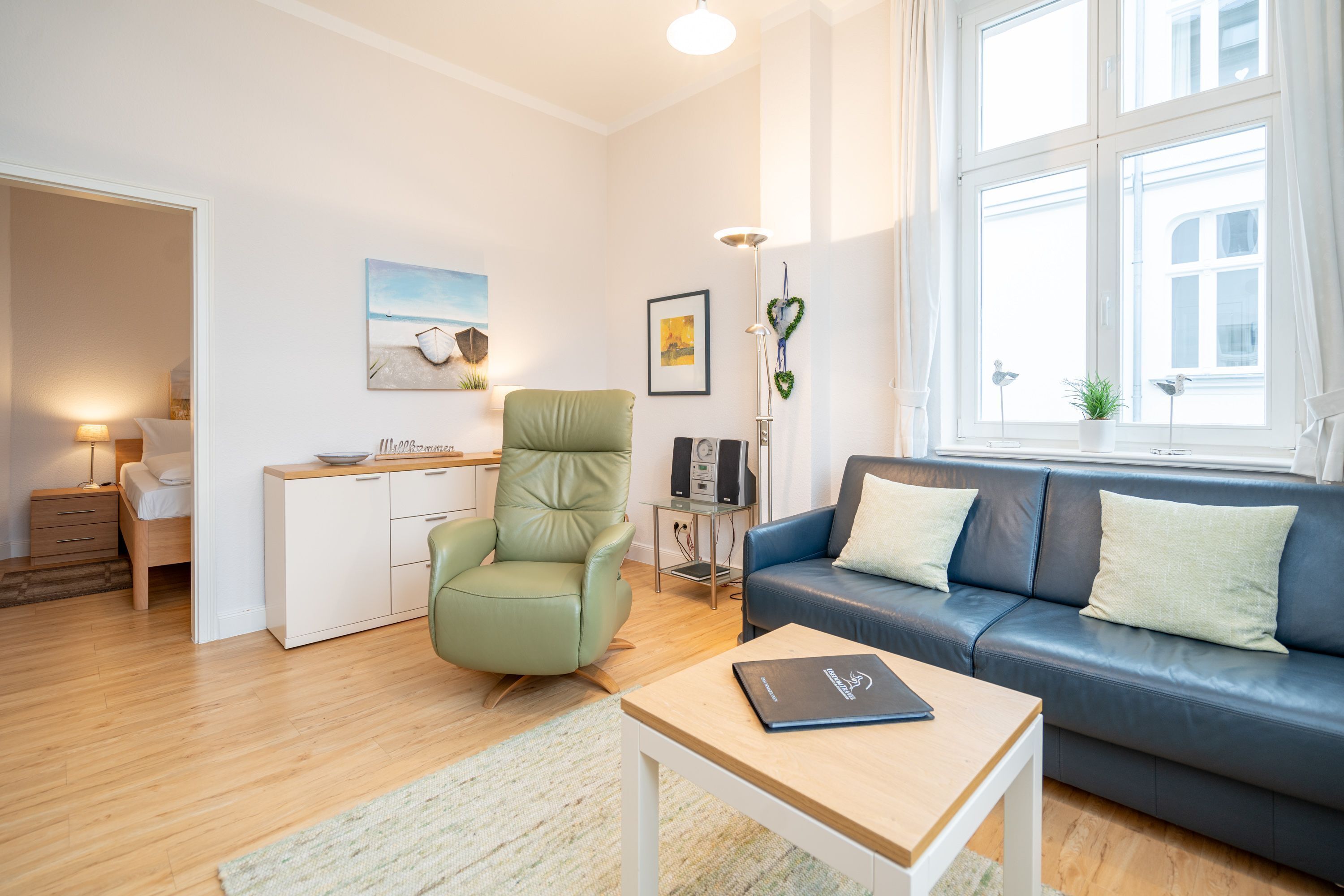Un salon moderne avec un canapé, un fauteuil vert, une petite table et un bureau.