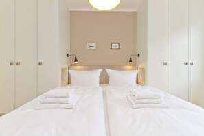 A double bed with white linens, two bedside lamps, and a neutral-colored wall with two small framed pictures.