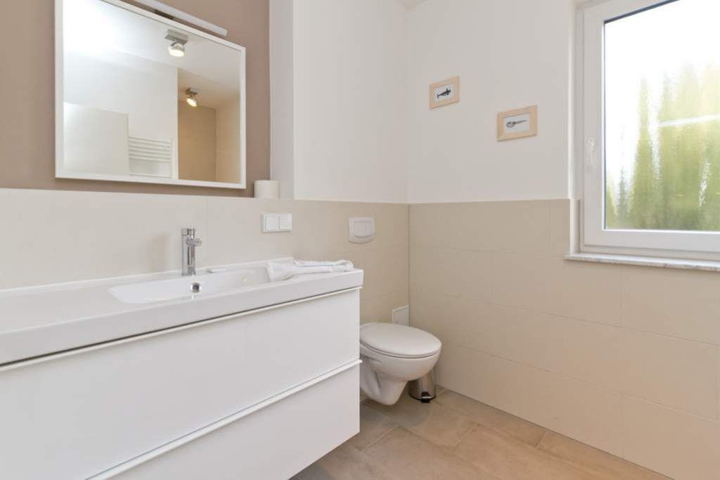 Een badkamer met een wit wastafelmeubel, een spiegel, een toilet en een raam.