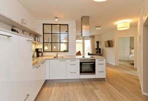 Une cuisine moderne avec des meubles blancs, une grande fenêtre et un four encastré.