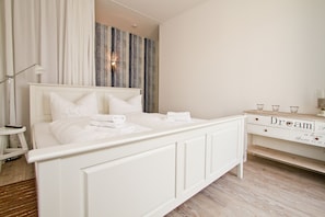 A white bed with pillows and a bedside table with a lamp and glasses.