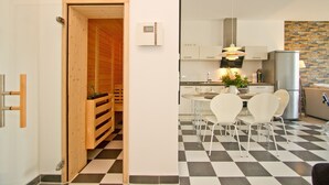 Una cuina moderna amb un paviment a quadradets, cadires blanques i una porta de sauna de fusta.