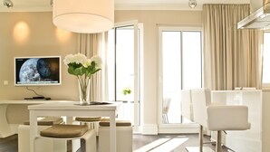 A modern, well-lit room with a dining area, a white sofa, and a TV on the wall.