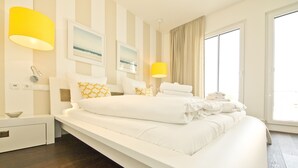 A modern hotel room with a large bed, two bedside lamps, a view of the outdoors, and a small bedside table with a bowl.