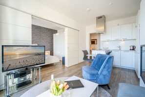 A modern living room with a flat-screen TV, a glass coffee table, and a blue chair. - Dünenpalais, App. 16 (Heringsdorf)