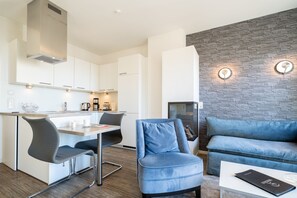 A modern kitchen with white cabinets, a built-in stove, and a dining area with a table and chairs. - Dünenpalais, App. 16 (Heringsdorf)