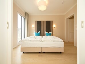 Ein Hotelzimmer mit einem großen Bett, zwei Wandleuchten, einem Vorhangfenster und einer Tür.