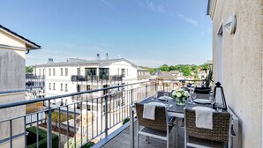 En balkon med et bord dækket til to, med udsigt over en gårdhave med bygninger og grønt.