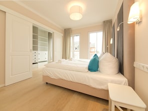 Un dormitorio con cama, mesita de noche blanca, vestidor y ventana con cortinas.