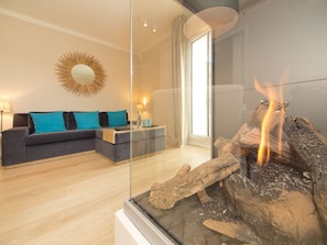 Una sala de estar moderna con chimenea de vidrio, un sofá con cojines verde azulado y un espejo grande en la pared.