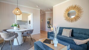 En moderne stue med en blå sofa, et rundt spejl med solstråle-udsmykning og et spiseområde med et hvidt bord og stole.