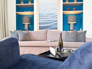 Un salon moderne avec un canapé beige, une table basse noire et un mur bleu agrémenté d’une grande fenêtre.