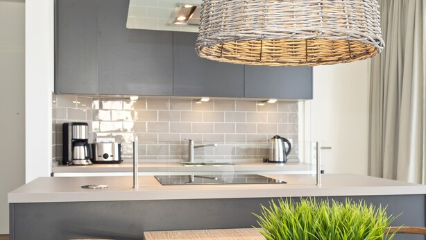 A modern kitchen with a central island, stainless steel appliances, and a woven light fixture. - Dünenpalais, App. 10 (Heringsdorf)