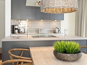 Une cuisine moderne dotée d’un îlot central, d’appareils électroménagers en acier inoxydable et d’un luminaire au design tressé.