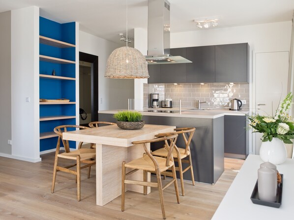 Une cuisine moderne avec un îlot central, des chaises en bois, un luminaire suspendu et une étagère bleue.