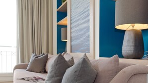 A modern living room with a beige sofa, grey cushions, a blue accent wall, and a large window with curtains. - Dünenpalais, App. 10 (Heringsdorf)