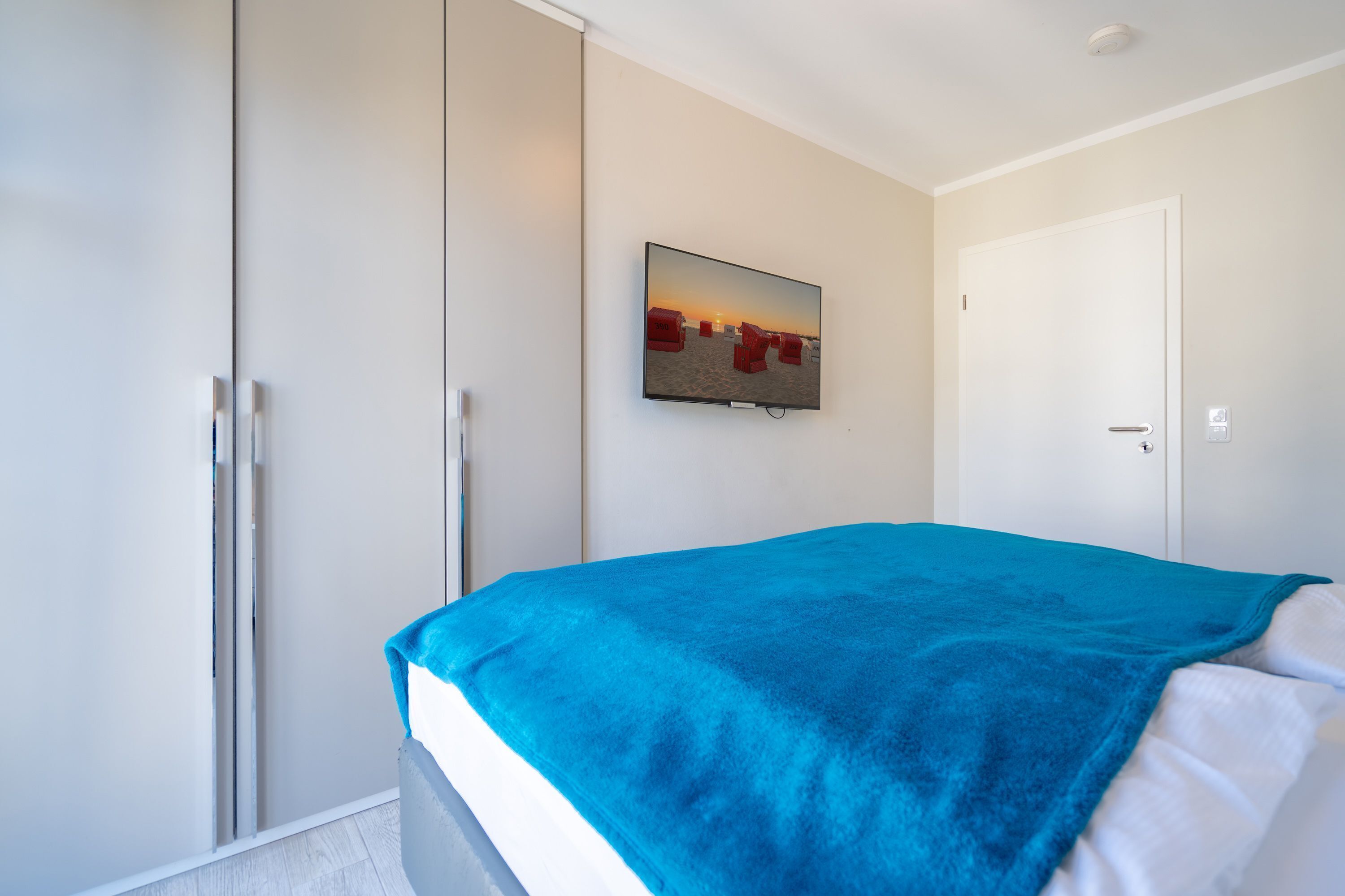 A bedroom with a bed, a television mounted on the wall, and a wardrobe.