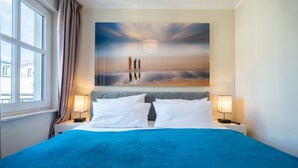 Una camera d'albergo con un letto grande, due comodini con lampade, un quadro raffigurante una spiaggia e una finestra con tende.