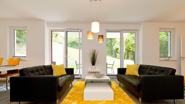 Ein modernes Wohnzimmer mit zwei schwarzen Sofas, einem gelben Teppich und einem weißen Couchtisch.