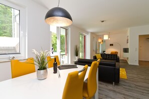 A modern living room with a black sofa, yellow chairs, and a dining table with a potted plant and wine bottle.