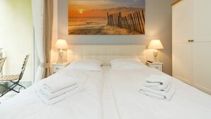 A hotel room with a large bed, two bedside lamps, a painting of a beach scene, and a wardrobe. - Villa Barbara, App. 09 (Heringsdorf)